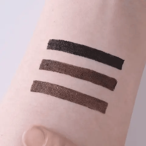 Three lines of black and brown makeup swatches on a person's arm.